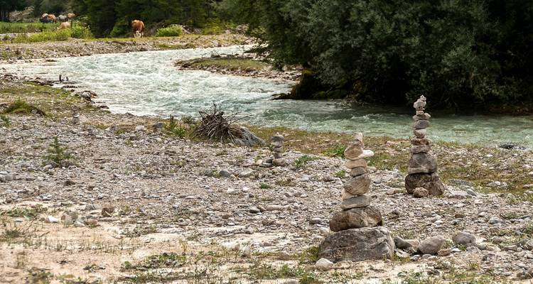 Fluss mit Steinmännchen und Bäumen in natürlicher Umgebung.