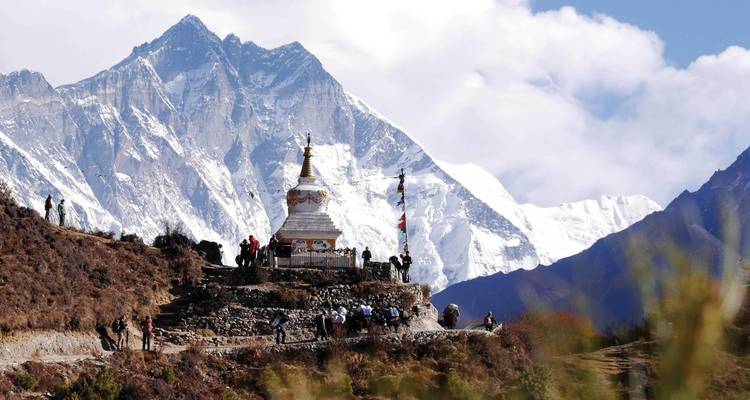 Groep mensen bij een stupa met de Himalaya op de achtergrond.