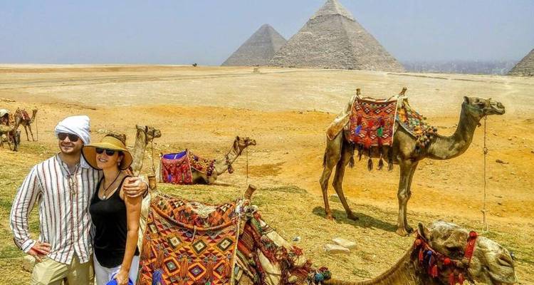 Touristes avec des chameaux et les pyramides en arrière-plan.