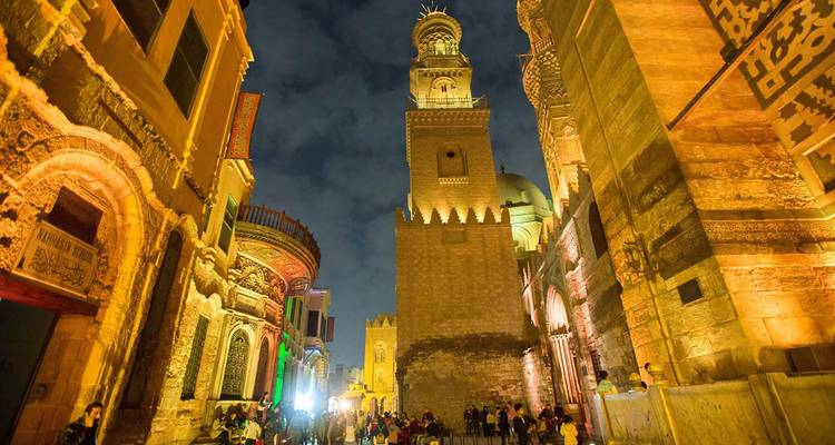 Scène nocturne d'une rue animée avec des bâtiments historiques illuminés.