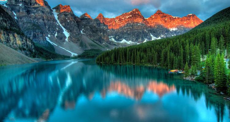 Stunning lake surrounded by forest and mountain peaks with a sunset glow.