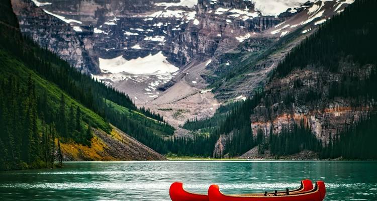 Rode kano op een turquoise meer te midden van torenhoge bergen.