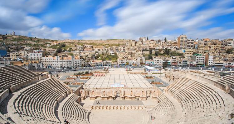 Wide angle of Amman's ancient Roman amphitheatre with modern city buildings climbing the hillside behind.