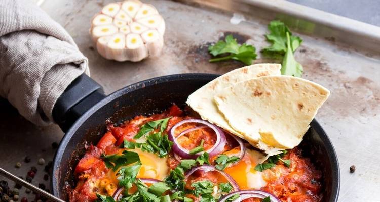 Pan shakshuka met garnituur en flatbread ernaast.