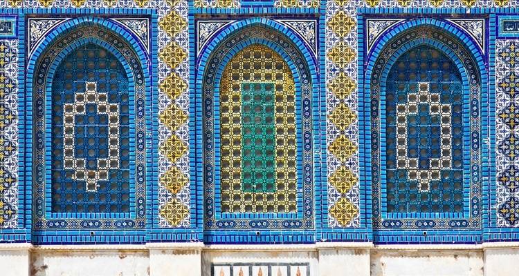 Close-up van ingewikkelde mozaïekpatronen in blauw en goud op een gebouwgevel.