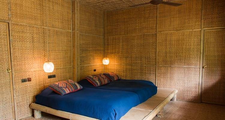 Interieur van een rustieke kamer met bamboe wanden en een tweepersoonsbed.