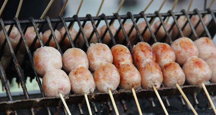 Gegrilde worstjes aan spiesen boven een houtskoolbarbecue.