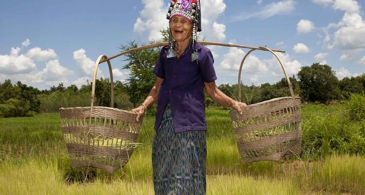 Persoon in traditionele kleding die manden draagt in een veld.