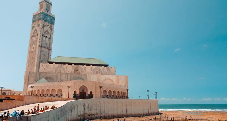 Vista marítima de la Mezquita Hassan II con visitantes sentados en la rampa junto al Océano Atlántico.