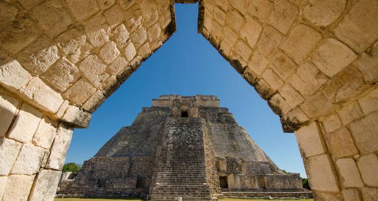 De Piramide van de Tovenaar in Uxmal perfect ingelijst door een stenen boog tegen een wolkenloze blauwe lucht.