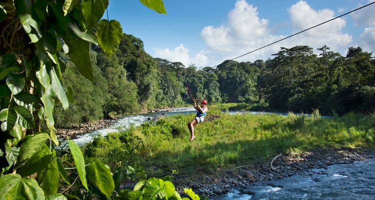 Aventurier faisant de la tyrolienne au-dessus d'une rivière de jungle au débit rapide entourée d'une forêt tropicale luxuriante.