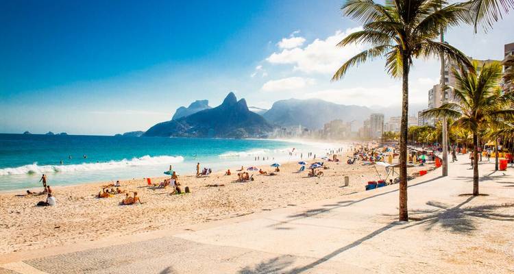 Iconic Ipanema Beach in Rio with sunbathers, surfers and Dois Irmãos peaks rising in the haze.