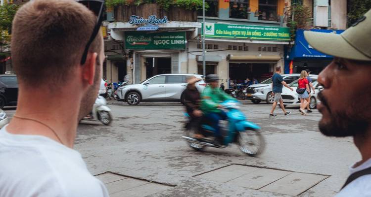 Travellers pause at a busy junction as a blurred motorbike speeds by in front of them.