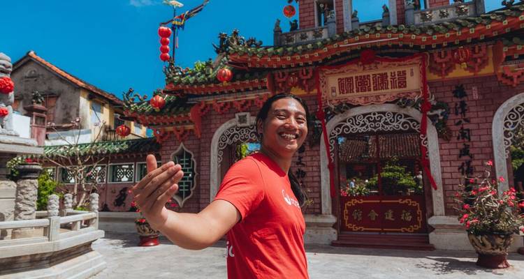 Smiling local guide gestures toward an ornate temple courtyard decorated with lanterns.