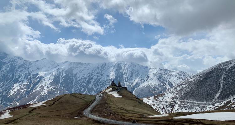 Chemin sinueux menant à une église devant des montagnes enneigées.