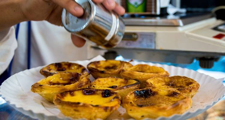 Des tartelettes à la crème custard Pastel de Nata fraîchement cuites saupoudrées de cannelle sur une assiette blanche.