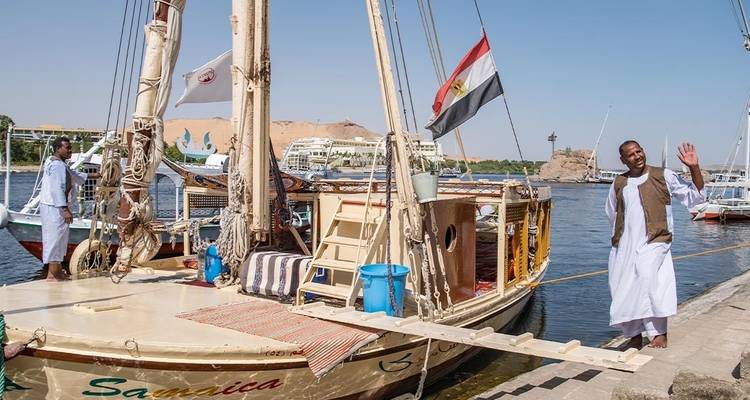 Menschen auf einem Boot mit ägyptischer Flagge in der Nähe eines Flussufers.