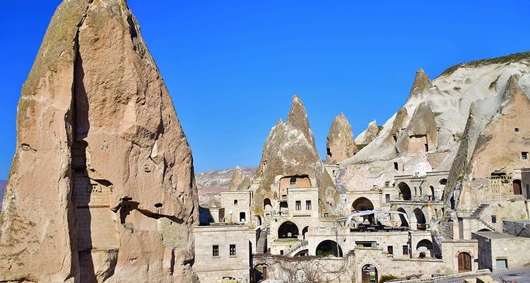 Höhlenwohnungen und Minarett vor blauem Himmel.