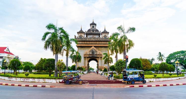 Ikonischer Wahrzeichen-Bogen mit umliegenden Tuk-Tuks und Palmen.