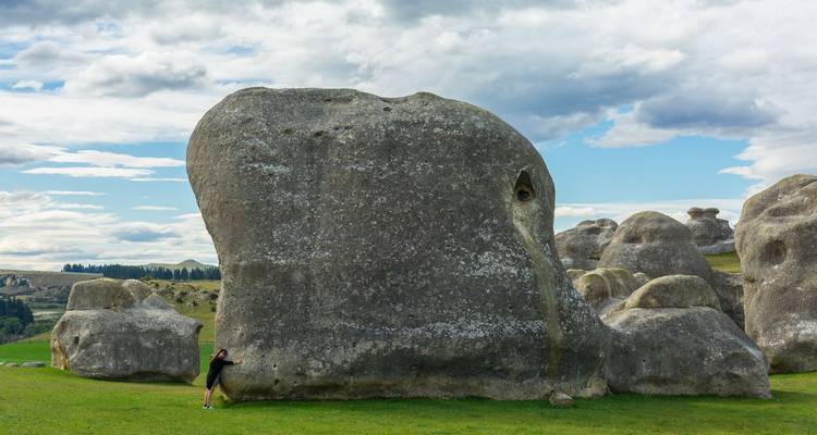 Un visitante empequeñecido por una enorme roca de caliza moldeada por el clima en un prado ondulante.