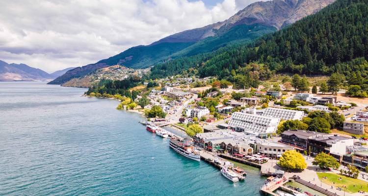 Vue aérienne d'une ville côtière avec des collines et des montagnes en arrière-plan.