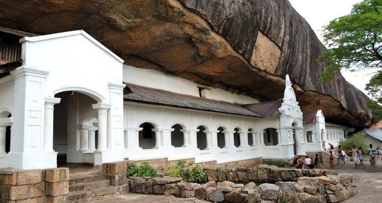 Templo blanco construido bajo una gran formación rocosa.