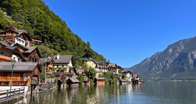 Malerische Holzhäuser von Hallstatt säumen das Seeufer unterhalb bewaldeter Berge und klarem Himmel.