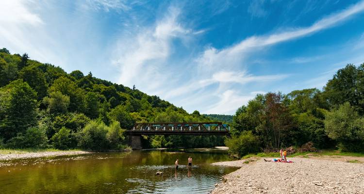 Famille se relaxant au bord d'une rivière avec un pont en arrière-plan.