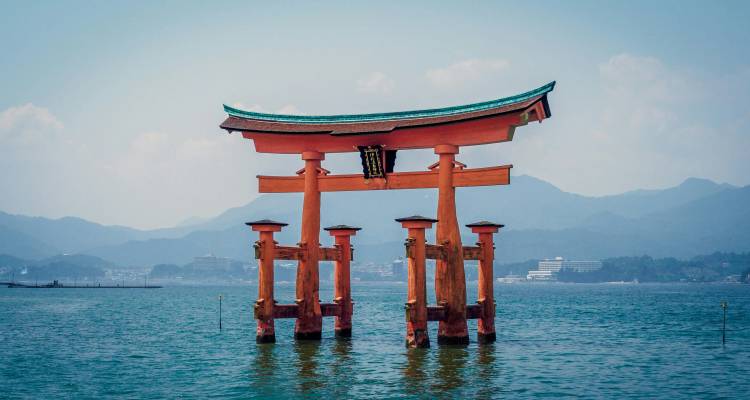 Vermiljoenrode torii poort van Itsukushima Shrine lijkt te zweven in kalme blauwe zee met mistige bergen erachter.
