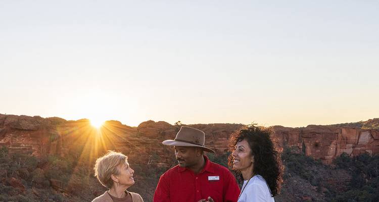 Guide chats with two visitors at sunrise with rugged canyon walls behind.