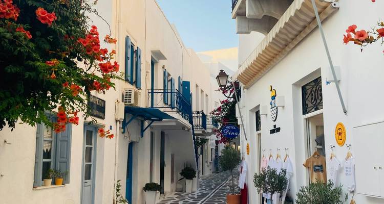 Calle estrecha empedrada con edificios blancos y buganvilla en un pueblo griego.