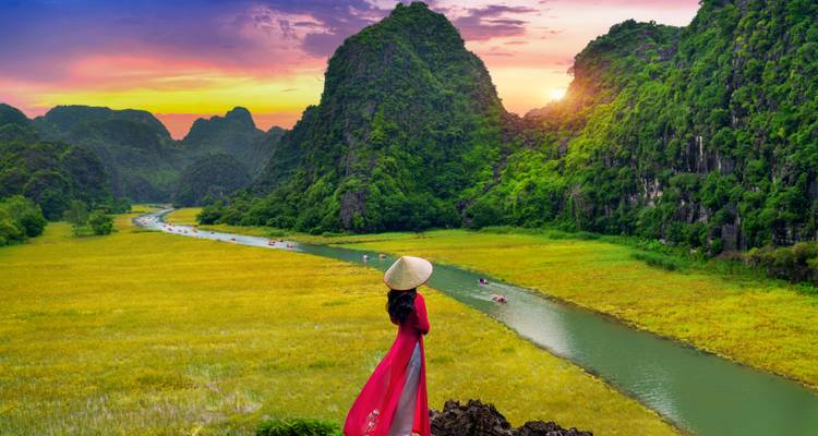 Woman in traditional dress looking over a scenic valley at sunset.