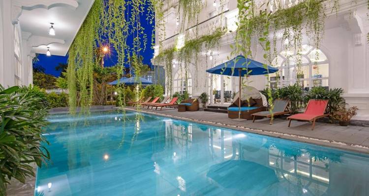 Hotelpool mit umgebender Begrünung und Liegestühlen bei Nacht.