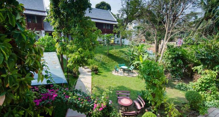 Ein malerischer Garten mit Tischen und üppigem Grün, umgeben von traditionellen Gebäuden.