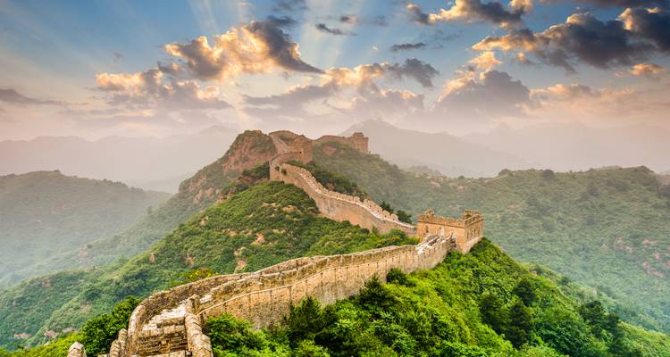 La Gran Muralla China extendiéndose sobre exuberantes colinas verdes bajo un cielo dramático.