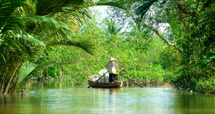 Person rowing a boat along a lush, green waterway.