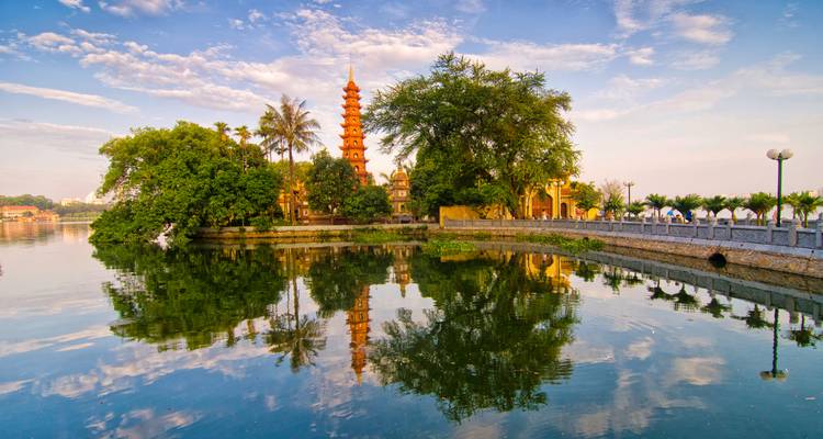 Tran Quoc Pagoda and lush trees reflect perfectly on Hanoi's West Lake in warm morning light.