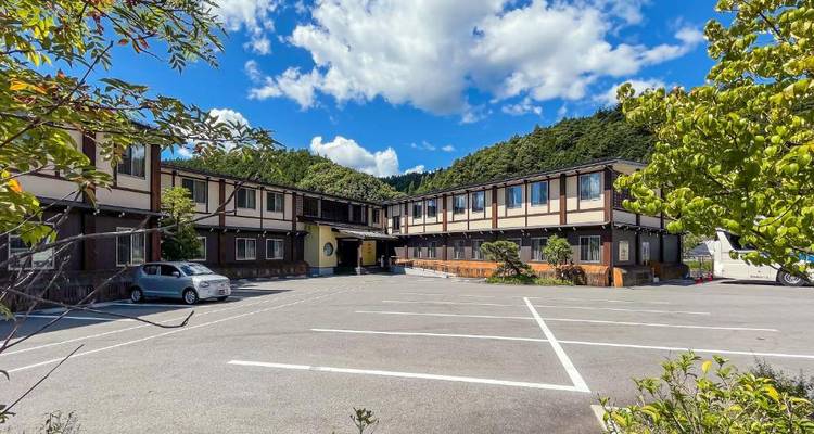 Edificio con área de estacionamiento, rodeado de vegetación.
