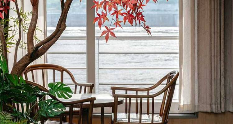 Kleine Sitzecke neben großem Fenster mit Flussblick, dekoriert mit roten Blättern und Pflanzen.