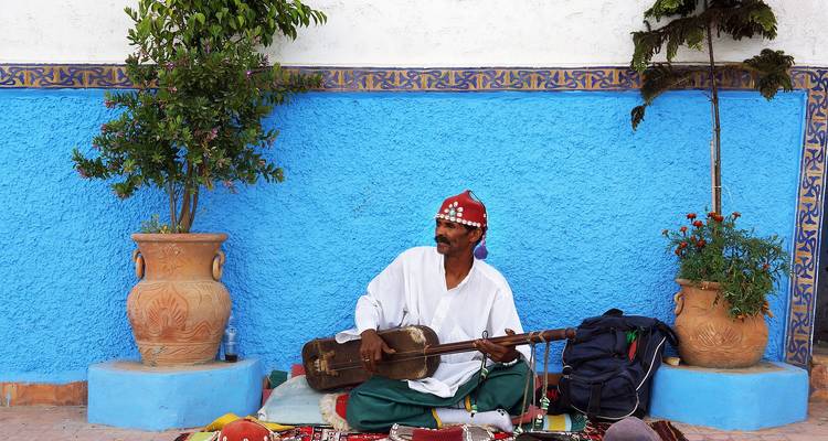 Musicien de rue jouant d'un instrument assis devant un mur bleu
