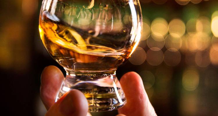 Primer plano de una mano sosteniendo una copa de whisky con fondo desenfocado.