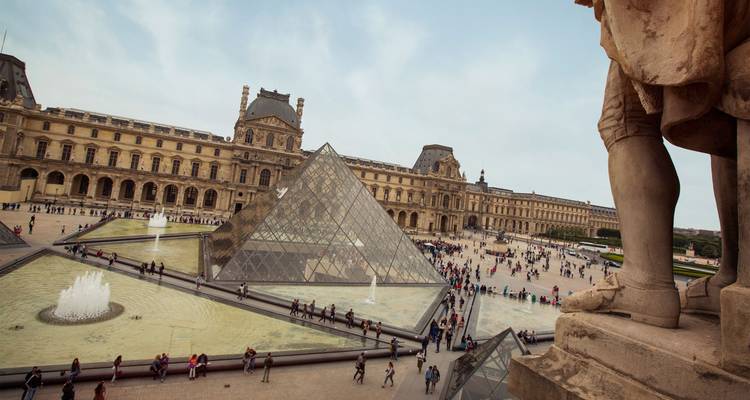 The Louvre Pyramid and palace courtyard bustle with visitors beside elegant fountains.