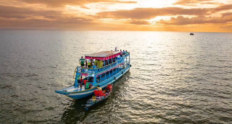 Des touristes sur un bateau dans des eaux calmes au coucher du soleil.