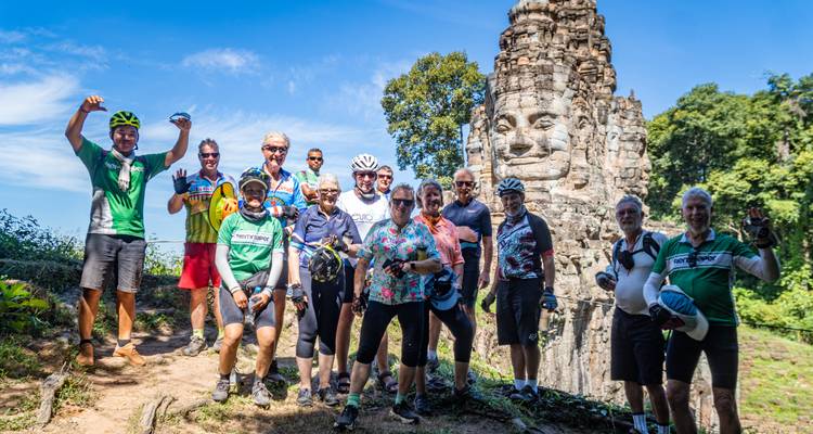 Groupe de touristes souriant devant une statue de visage en pierre ancienne.