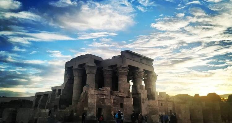 Temple ruins silhouetted against dramatic sky during sunset.