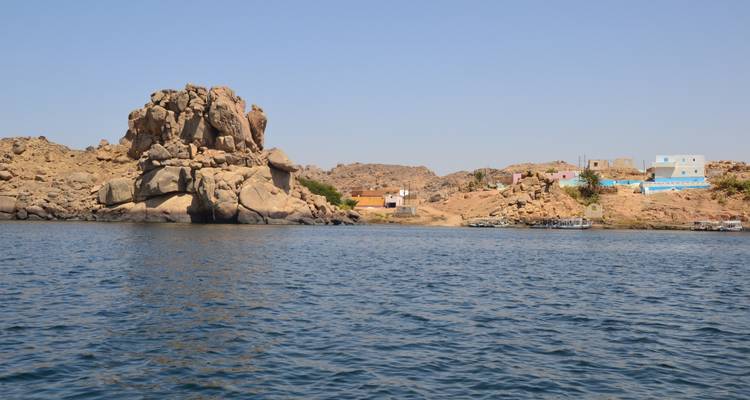 Lakeside scene with rocky formations and distant village.