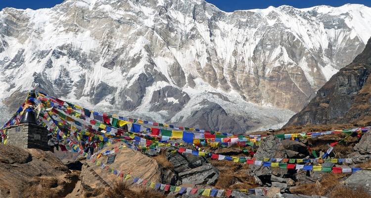 Gebetsfahnen, die über felsiges Gelände gespannt sind, mit Bergen im Hintergrund