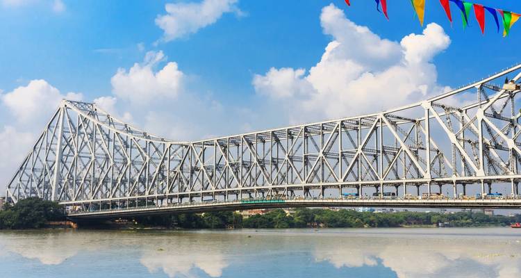 Een stalen brug die een kalme rivier overspant met een blauwe lucht.
