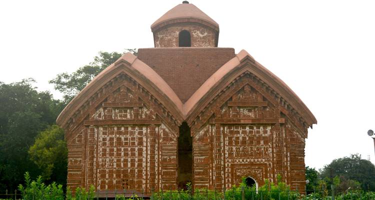 Een kleine, historische terracotta tempel omringd door groen.
