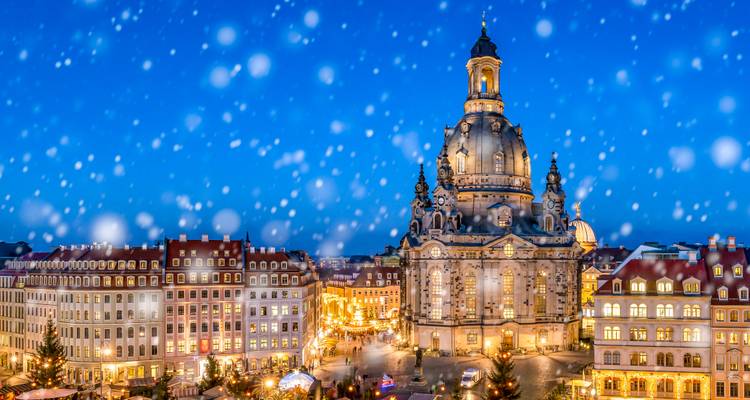 Snowy festive evening view of Dresden’s Frauenkirche and old town market lights under a blue sky